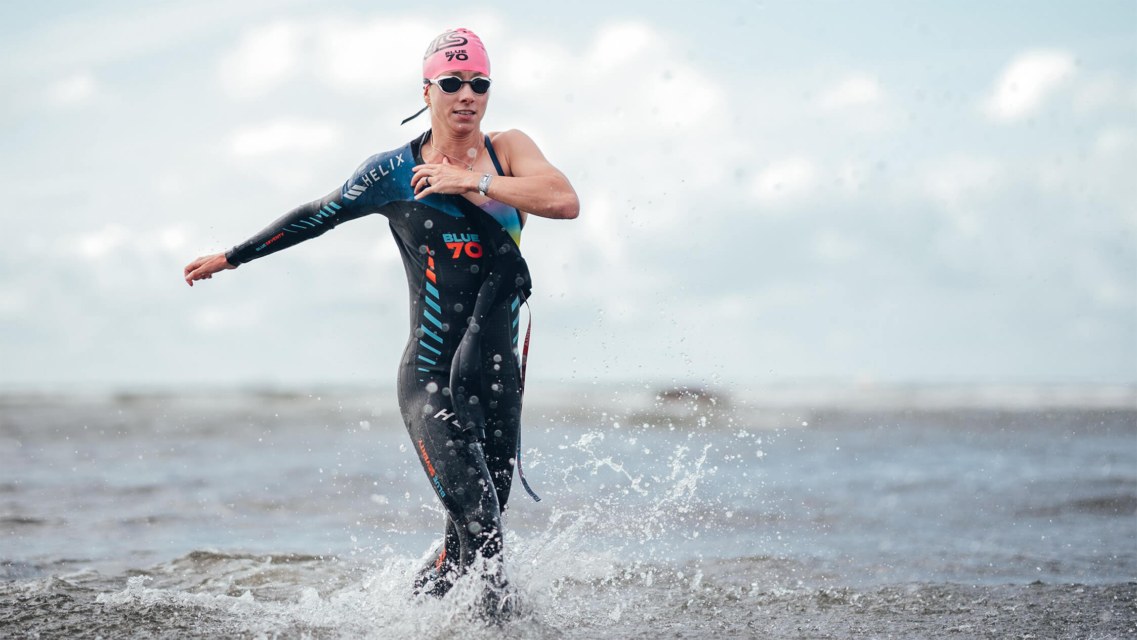Person in a wetsuit and swim cap running out of the water on a beach